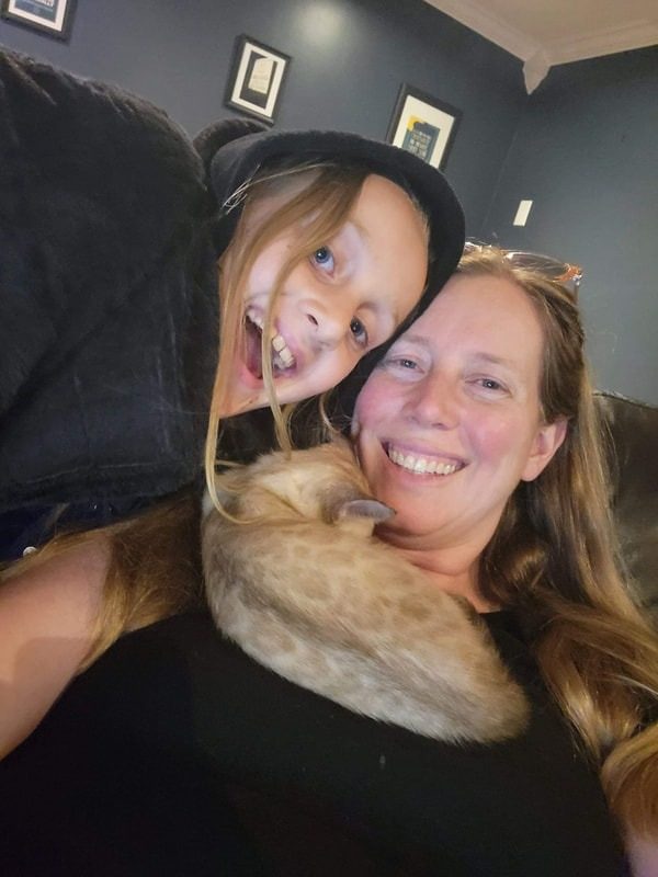 A mother and child cheek to cheek with their Bengal draped around them